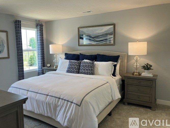 A bedroom with a large bed, two lamps, and a painting on the wall.