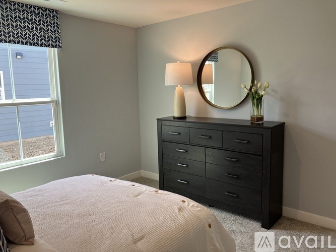 A bedroom with a large bed, a dresser with a mirror, and a window with a view of a blue house.