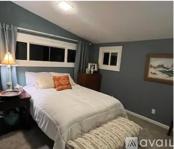 A bedroom with a white bed and a lamp on a side table.