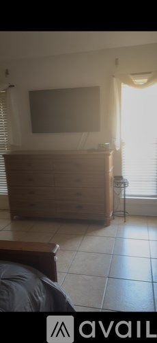 A wooden dresser with a flat screen TV mounted above it in a room with a window.