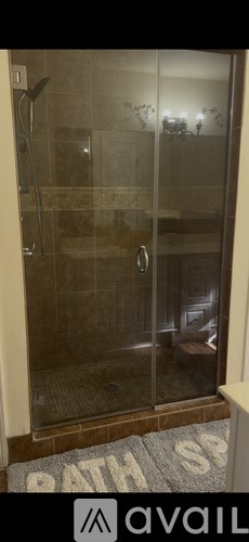 A bathroom with a glass shower door and a bath mat on the floor.