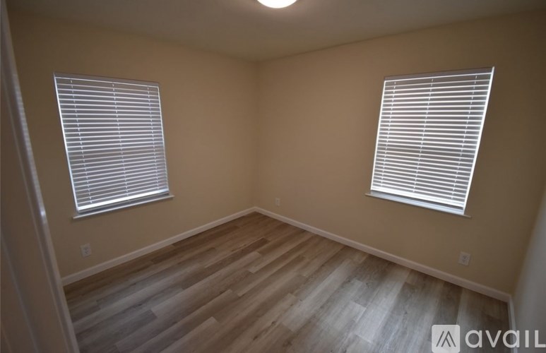 A room with wooden floors and two windows with blinds.