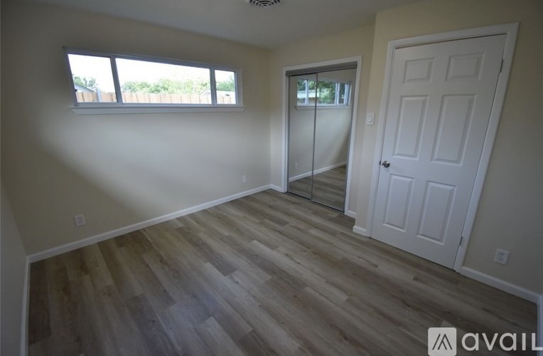 A room with a white door and a window with a view of trees.