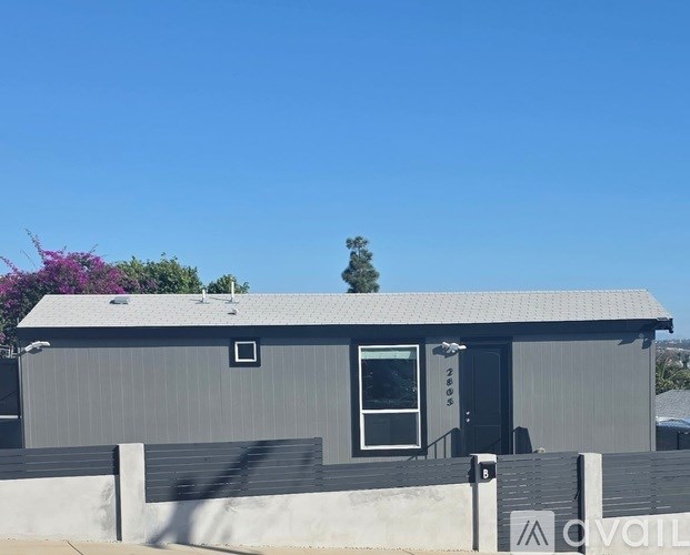A grey building with a black door and a window is in front of a blue sky.