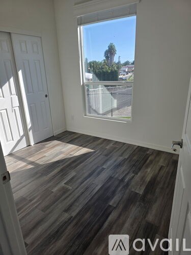 A room with wooden flooring and a window overlooking a parking lot.