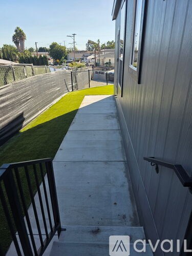 A concrete walkway with a metal railing on the left and a grey building on the right.