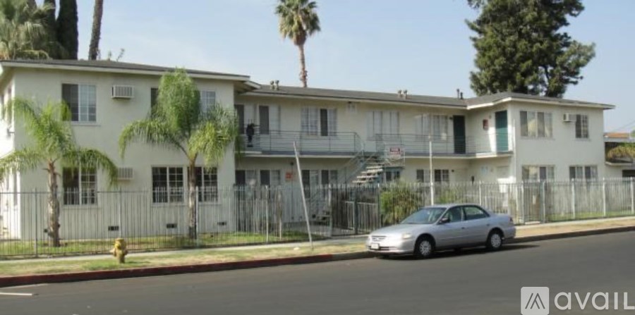 A silver car is parked in front of a white two-story house with a balcony.