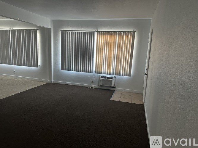 A room with a window covered by blinds and a black carpet.
