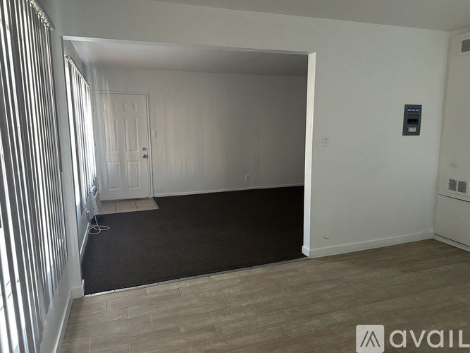 A room with a door, a window with blinds, and a wall-mounted device.