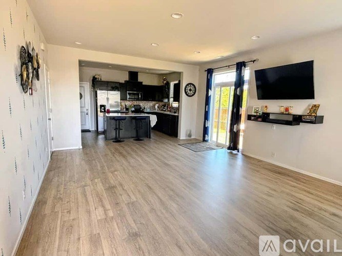 A spacious room with wooden flooring and a kitchen area in the background.