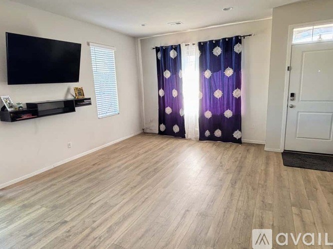 A living room with a flat screen TV mounted on the wall and a purple curtain with white flowers.