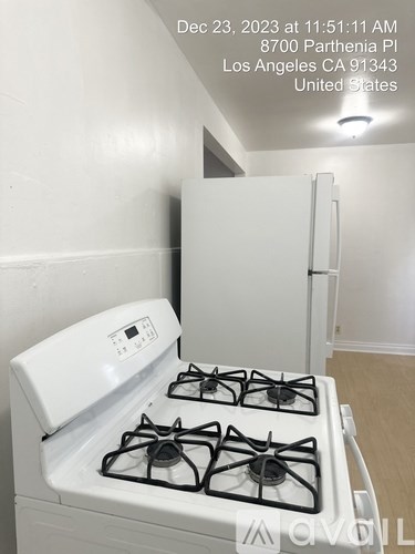 A white gas stove in a kitchen with a white wall and a white fridge.
