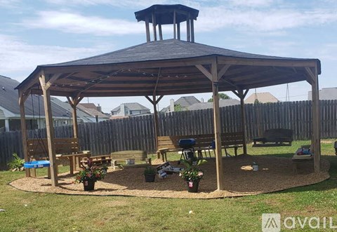 A gazebo with a black roof and wooden pillars is surrounded by a wooden fence.