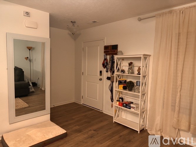 A room with a white door, a white shelf with various items, and a mirror on the wall.
