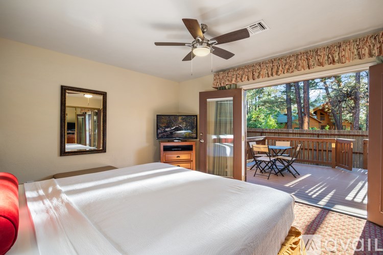 A bedroom with a large bed and a balcony overlooking a wooded area.
