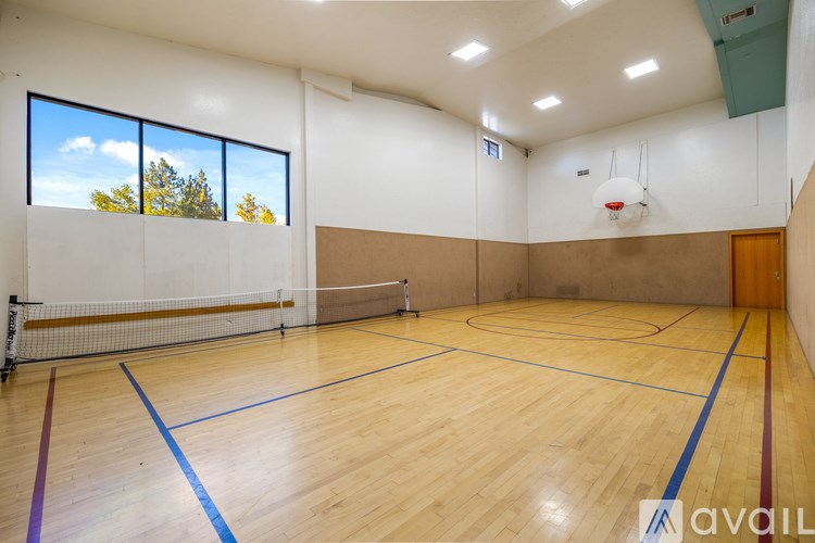 A large indoor basketball court with wooden flooring and a white wall with windows.