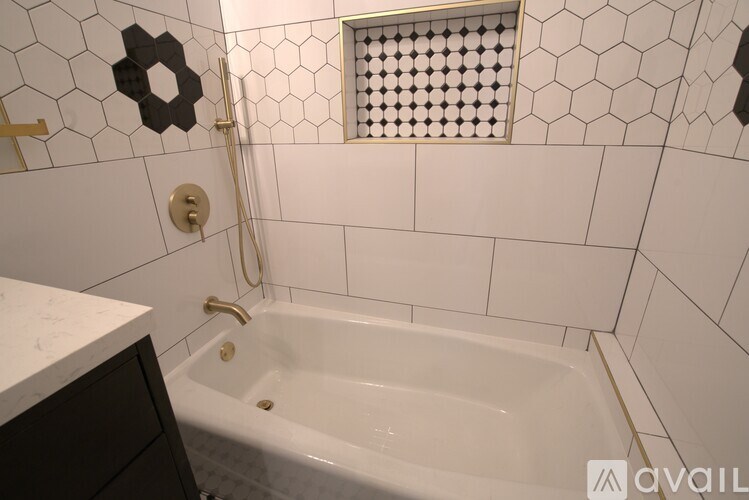 A white tiled bathroom with a white tub and a window with a hexagonal pattern.