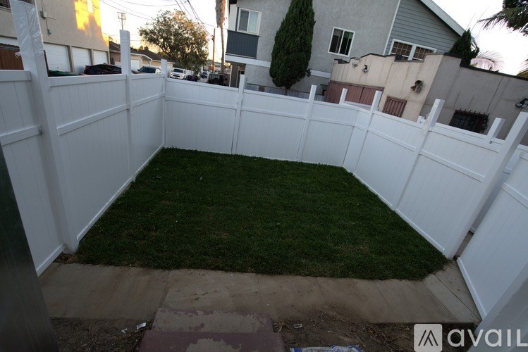 A backyard with a white fence and green grass.