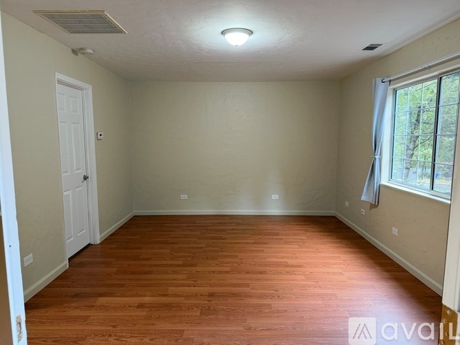 A room with wooden flooring and a window with a view of trees.