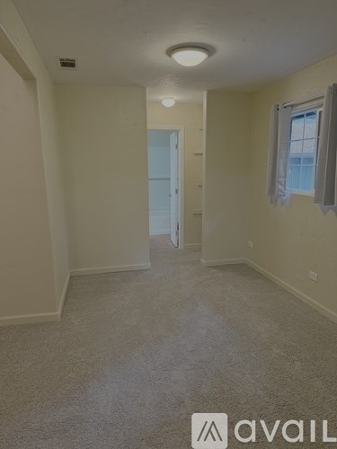 A room with a carpeted floor and a window with white curtains.