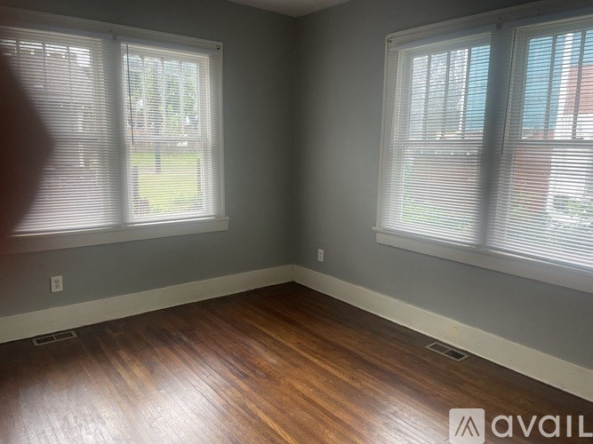 A room with wooden floors and two windows with blinds.