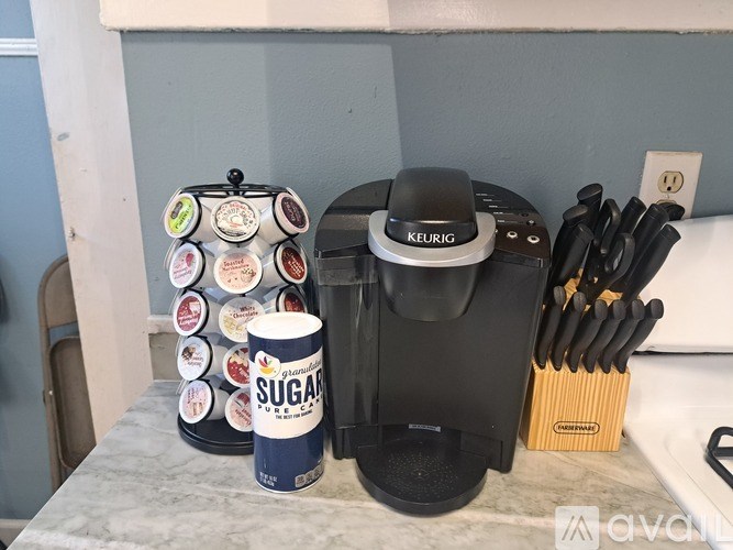 A Keurig coffee maker sits on a counter with a can of sugar and a set of knives.