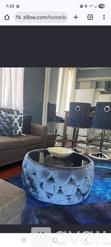 A modern living room with a round blue ottoman in the center.