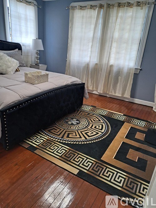 A bedroom with a black bed and a Greek key patterned rug.