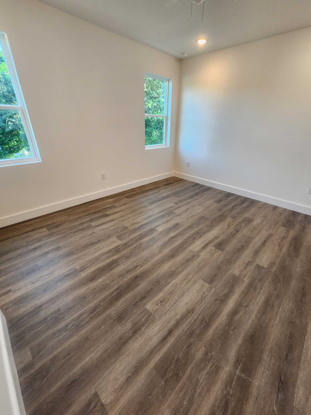 A room with wooden flooring and two windows.