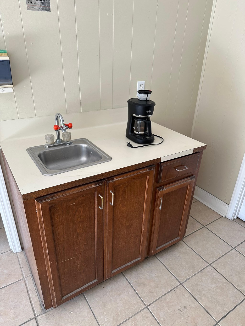 A coffee maker is on a counter with a sink.