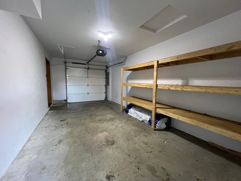 A room with a white ceiling and a white wall with a wooden shelf.
