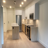 A kitchen with a refrigerator, sink, and cabinets.