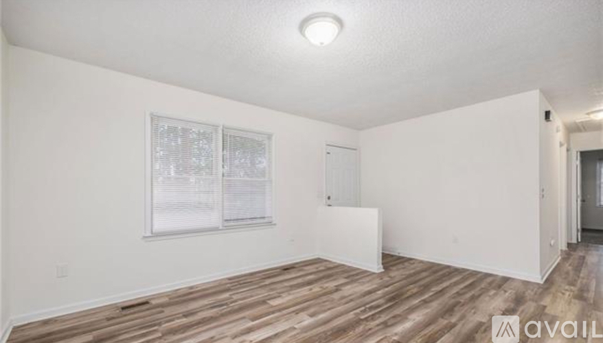 A room with wooden flooring and white walls, with a window and a door visible.
