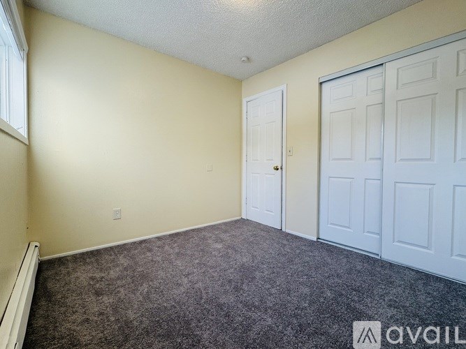 A room with a carpeted floor, a white door, and a white closet with multiple doors.