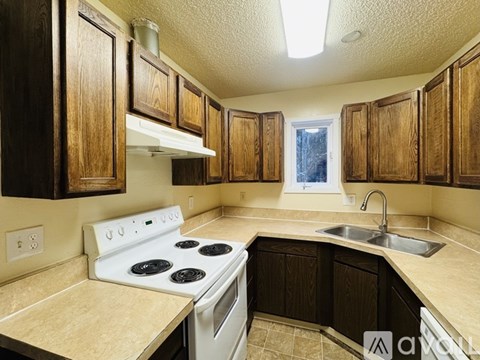 A kitchen with a white stove top oven and wooden cabinets.