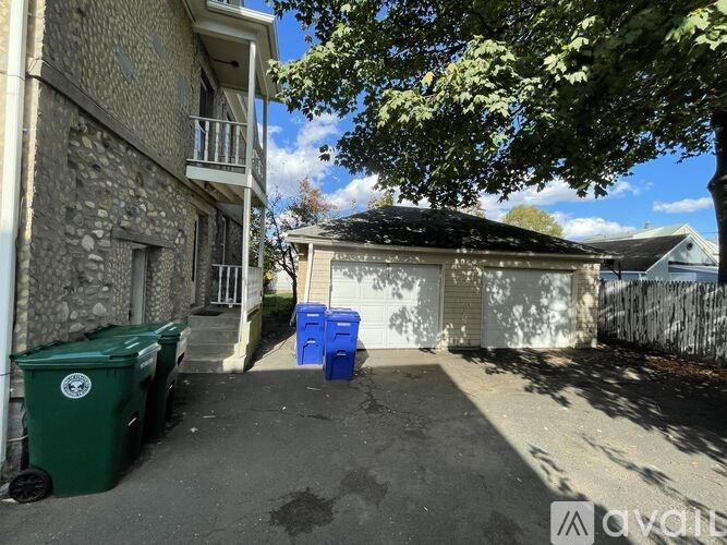 A green trash bin sits on a driveway in front of a house.