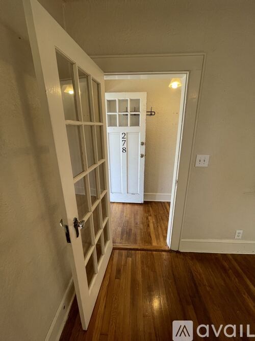 A white door with a glass window and a handle is in a room with wooden floors.