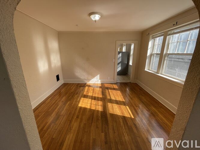 A room with wooden flooring and a window letting in sunlight.