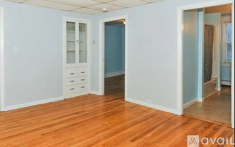 A room with wooden floors and white walls, with a cabinet and drawers in the corner.
