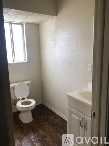 A bathroom with a toilet, sink and wood flooring.