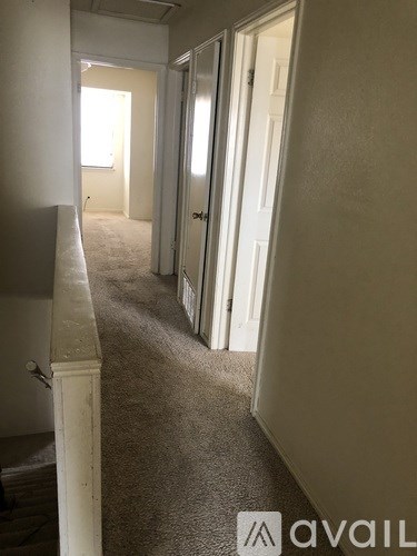 A hallway with carpeted floors and white walls leading to a door.