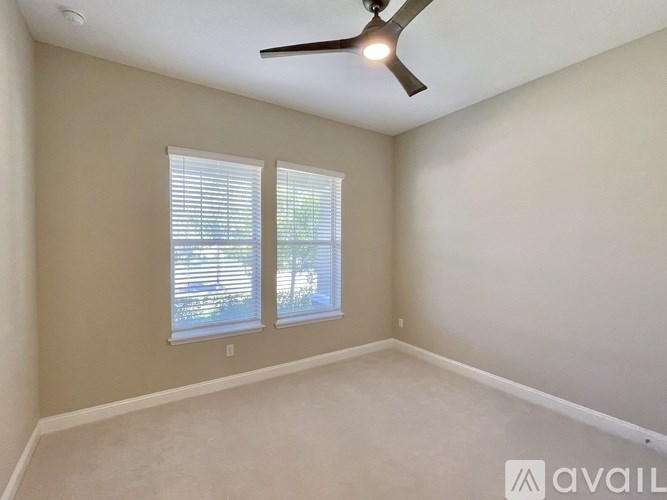 A room with a ceiling fan and two windows.