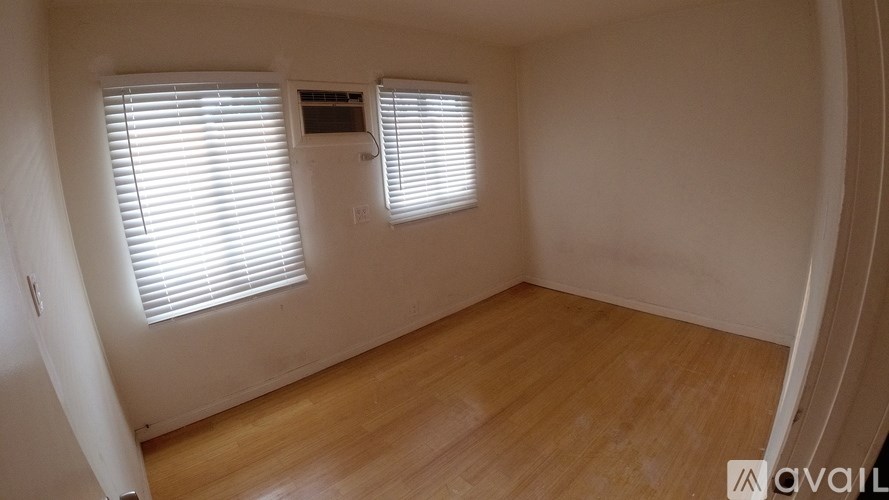 A room with wooden flooring and two windows with blinds.