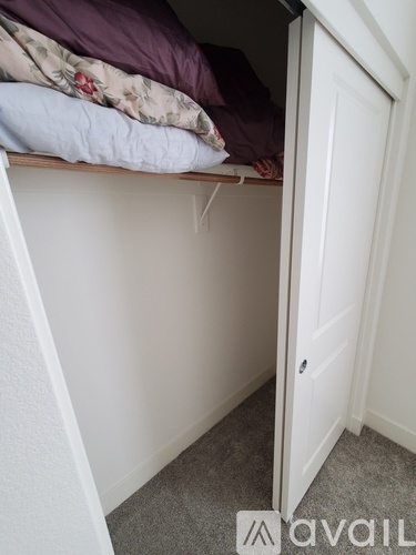 A white door is in a white room with a bed in the corner.