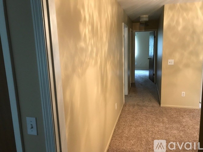 A hallway with beige walls and carpeting, leading to a door at the end.