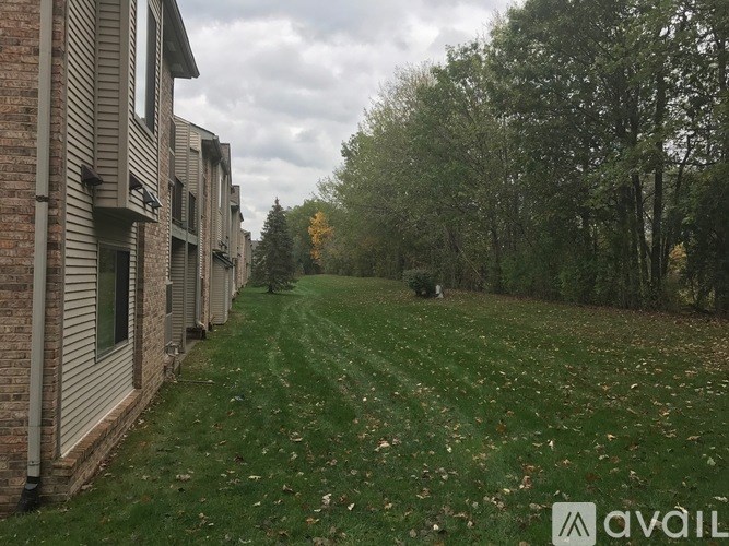 A grassy pathway leads through a wooded area with a row of houses on the left.