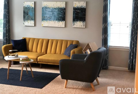 A living room with a yellow sofa, a black chair, and two abstract paintings on the wall.