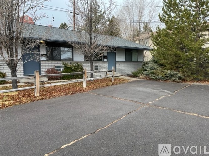 A house with a grey roof and a blue door is surrounded by a wooden fence and a driveway.