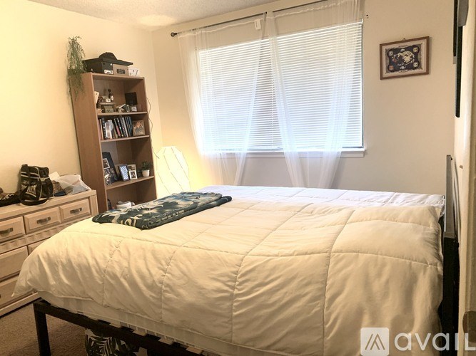 A bedroom with a bed, a bookshelf, and a window with blinds.