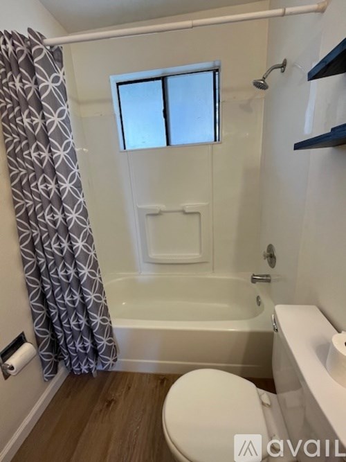 A bathroom with a toilet, a bathtub with a shower curtain, and a window.